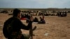 FILE - A member of U.S.-backed Syrian Democratic Forces (SDF) watches over people who were evacuated out of the last territory held by Islamic State militants, outside Baghouz, Syria, March 5, 2019.