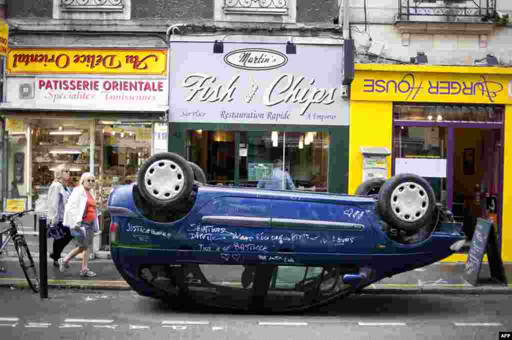 A car is seen parked on its roof in front of shops with upside down signs in a street of Nantes, western France, as part of the &quot;A journey to Nantes&quot; (Le Voyage a Nantes) art festival.
