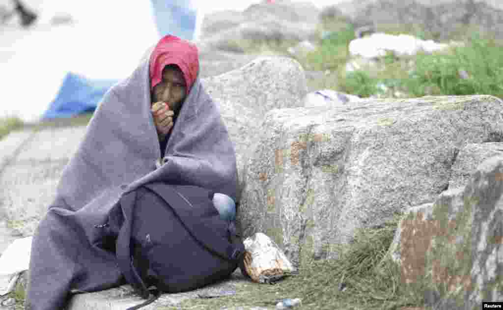 Seorang migran memakai selimut sambil makan apel di kamp darurat di tempat penyeberangan perbatasan di Nickelsdorf, Austria (6/9). (Reuters/Srdjan Zivulovic)
