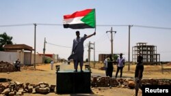 FILE - A Sudanese protester holds a national flag as he stands on a barricade along a street, in Khartoum, Sudan, June 5, 2019.