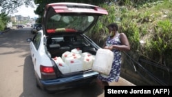 Une femme charge dans un taxi des conteneurs remplis d'eau recueillie dans une source naturelle à Libreville, au Gabon, le 2 février 2021.