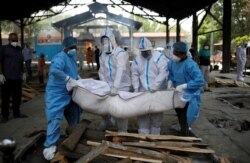 Health workers and relatives wearing personal protective equipment (PPE) carry the body of a man, who died from COVID-19, at a crematorium in New Delhi, India, Apr. 21, 2021.