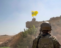 FILE - A U.S. soldier oversees members of the Syrian Democratic Forces as they demolish a Kurdish fighters' fortification and raise a Tal Abyad Military Council flag over the outpost as part of the "safe zone" near the Turkish border, Sept. 21, 2019.