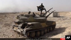 Militan ISIS berdiri di atas tank yang direbut dari pasukan pemerintah Suriah dan membentangkan bendara kelompoknya di kota al-Qaryatayn, sebelah barat daya Palmyra, Suriah bagian tengah.