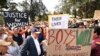 Perdana Menteri Australia Anthony Albanese (mengenakan topi dan berdiri di samping poster) menghadiri aksi demo, yang menyerukan penghentian kekerasan terhadap perempuan, di Canberra, pada 28 April 2024. (Foto: Lukas Coch/AAP Image via AP)