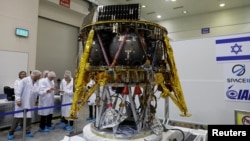 Israeli scientists stand next to an unmanned spacecraft which an Israeli team plans to launch into space at the end of the year and to land it on the moon next year, in Yahud, Israel, July 10, 2018.