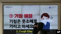 People wearing face masks pass by an electric screen about precautions against the illness COVID-19 in Seoul, South Korea, Tuesday, Feb. 18, 2020. 