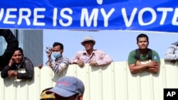 Cambodian workers look through a partition of a construction site below a banner which reads "Where is my vote" as supporters of opposition Cambodia National Rescue Party gather in Phnom Penh, Cambodia, Saturday, Sept. 7, 2013.
