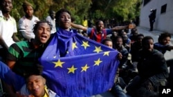 Un migrant portant un drapeau de l'Union européenne assis par terre avec d'autres après avoir pris d'assaut une clôture pour entrer dans l'enclave espagnole de Ceuta, Espagne, 17 février 2017.