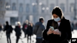Žena nosi zaštitnu masku dok gleda u svoj telefon, Milan, Italija, 24. februar 2020.