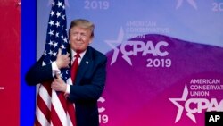 Presiden Donald Trump memeluk bendera AS saat dia tiba untuk berpidato pada Konferensi Tahunan Tindakan Politik Konservatif, Oxon Hill, Md., 2 Maret 2019.