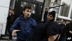 A civilian, left, and a security officer beat a protester as riot police use water cannons to disperse people protesting the detentions of 12 lawmakers from pro-Kurdish Peoples' Democratic Party, or HDP, in Istanbul, Nov. 5, 2016.
