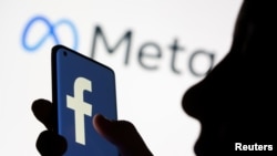 FILE - A woman holds a smartphone with the Facebook logo in front of a display of Facebook's parent company logo Meta in this illustration photo taken Oct. 28, 2021.