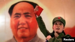 FILE - A Chinese, dressed as a Red Guard and holding a "Little Red Book" (quotations of Chairman Mao), performs in front of a portrait of the late Chairman Mao Zedong at a restaurant named "Red Classic" in Beijing.