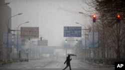 A man wears a mask as he walks across an empty intersection during the morning rush hour as snow falls in Beijing, Feb. 14, 2020. China on Friday reported another sharp rise in the number of people infected with a new virus and the death toll near 1,400.