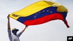 FILE - A masked anti-government protester waves a Venezuelan flag during protests in Caracas, Venezuela, May 1, 2019. 