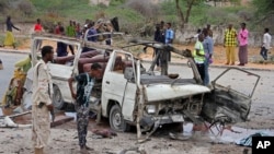 Seorang tentara Somalia (kiri) berdiri di dekat reruntuhan minibus yang hancur akibat serangan bom dekat kompleks Kementerian Pertahanan di Mogadishu, Somalia, 9 April 2017. (AP Photo/Farah Abdi Warsameh)