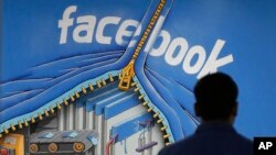 FILE - A Facebook employee walks past a sign at Facebook headquarters in Menlo Park, California in 2013.