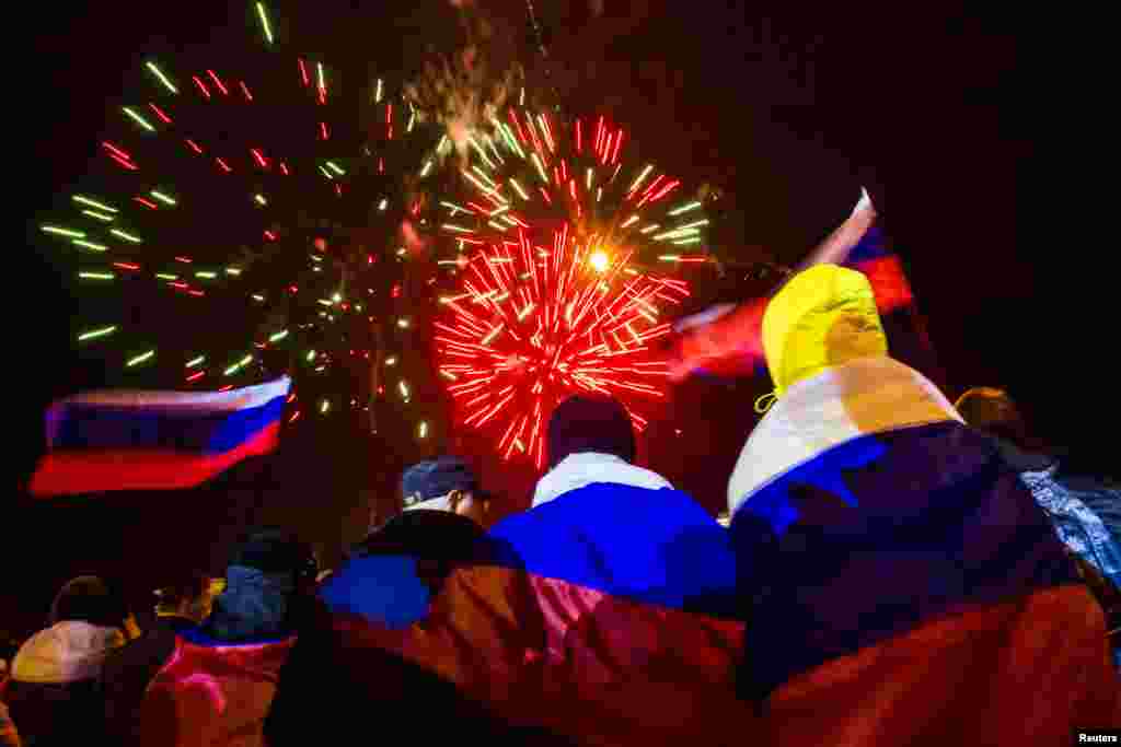 People wrapped in Russian flags watch fireworks during celebrations after the preliminary referendum results were announced in Lenin Square in the Crimean capital Simferopol, March 16, 2014. 