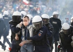 Polish police in riot gear detain protesters angry over new restrictions aimed at fighting the coronavirus pandemic, in Warsaw, Oct. 24, 2020.