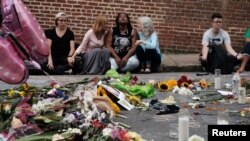 Women sit by an impromptu memorial of flowers commemorating the victims at the scene of the car attack on a group of counterprotesters during the "Unite the Right" rally as people continue to react to the weekend violence in Charlottesville, Va., Aug. 14,