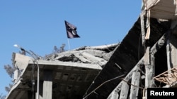 FILE - A flag of Islamic State militants is seen above a destroyed house in Raqqa, Syria, Oct. 18, 2017.