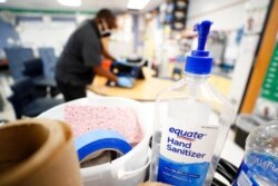 Hand sanitizer sits on a cart as Des Moines Public Schools custodian Tracy Harris cleans a chair at Brubaker Elementary School, July 8, 2020, in Des Moines, Iowa.