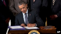 Surrounded by Cabinet officials and members of Congress, President Barack Obama signs H.R. 2146 Defending Public Safety Employees’ Retirement Act and H.R. 1295 Trade Preferences Extension Act of 2015 during a ceremony in the East Room of the White House, June 29, 2015.