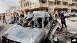 Warga menginspeksi sebuah mobil yang hancur akibat serangan bom dekat pintu gerbang iZona Hijau di Baghdad, Irak (19/3).