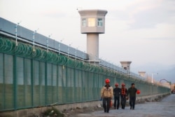 FILE - Workers walk by the perimeter fence of what is officially known as a vocational skills education center in Dabancheng, Xinjiang, China, Sept. 4, 2018.