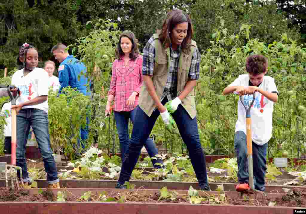 First Lady Michelle Obama, center, encourages a youngster with a pitchfork as they harvest vegetables in the White House Kitchen Garden, Oct. 6, 2016.
