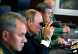FILE - Russian President Vladimir Putin, center, Defense Minister Sergei Shoigu, left, and Chief of the General Staff of the Russian Armed Forces Valery Gerasimov, right, watch a military exercise at a training ground at the Luzhsky Range, near St. Petersburg, Russia, Sept. 18, 2017.