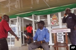 A health worker takes a man's temperature, center, before his is allowed to enter into a government building, with a message, right, reading "Kindly wash your hands before entering" the building in Monrovia, Liberia, Jan. 14, 2016.