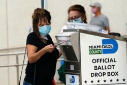 FILE - An election worker places a vote-by-mail ballot into an official ballot drop box outside of an early voting site in Miami, Florida, Oct. 19, 2020.
