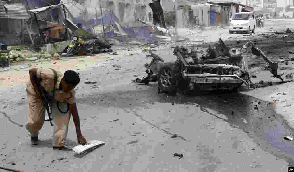 A Somali soldier picks up debris near the wreckage of car bomb in Mogadishu, Feb,13, 2014.