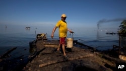A fisherman collects water contaminated with oil from Maracaibo Lake in Cabimas, Venezuela, Aug. 20, 2018. The fisherman will use the water to clean fish. Broken down oil platforms span the vast lake, with downwind shores soaked in oil.