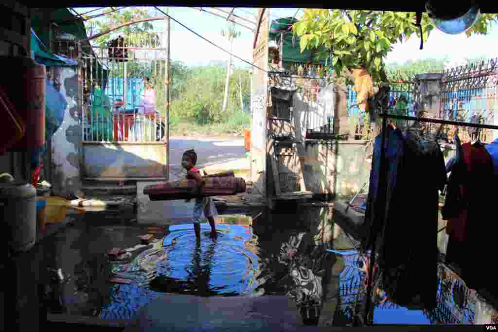 ក្មេងស្រី​ម្នាក់ ឈរ​កាន់​កន្ទេល​ក្នុង​ទឹក​ដែល​លិច​នៅ​មុខ​ផ្ទះ​របស់​លោក ឃឹន សុវាត ដែល​ស្ថិត​នៅ​ក្នុង​តំបន់​បឹងកក់ ក្នុង​ទីក្រុង​ភ្នំពេញ​នៃ​ប្រទេស​កម្ពុជា នៅ​ថ្ងៃ​ទី​១៣ ខែ​វិច្ឆិកា ឆ្នាំ​២០១៤។ (នូវ ពៅលក្ខិណា)