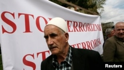 FILE - A Kosovo-Albanian man stands in front of a banner during a protest with the slogan "Stop Terrorism" in Pristina, Kosovo, April 24, 2012. A court in Pristina on Thursday sentenced seven men convicted of terror charges.