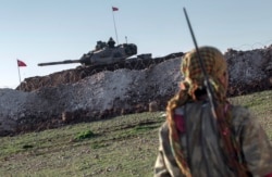FILE - A Syrian Kurdish militia member of the YPG patrols near a Turkish army tank in Esme village in Aleppo province, Syria, Feb. 22, 2015.