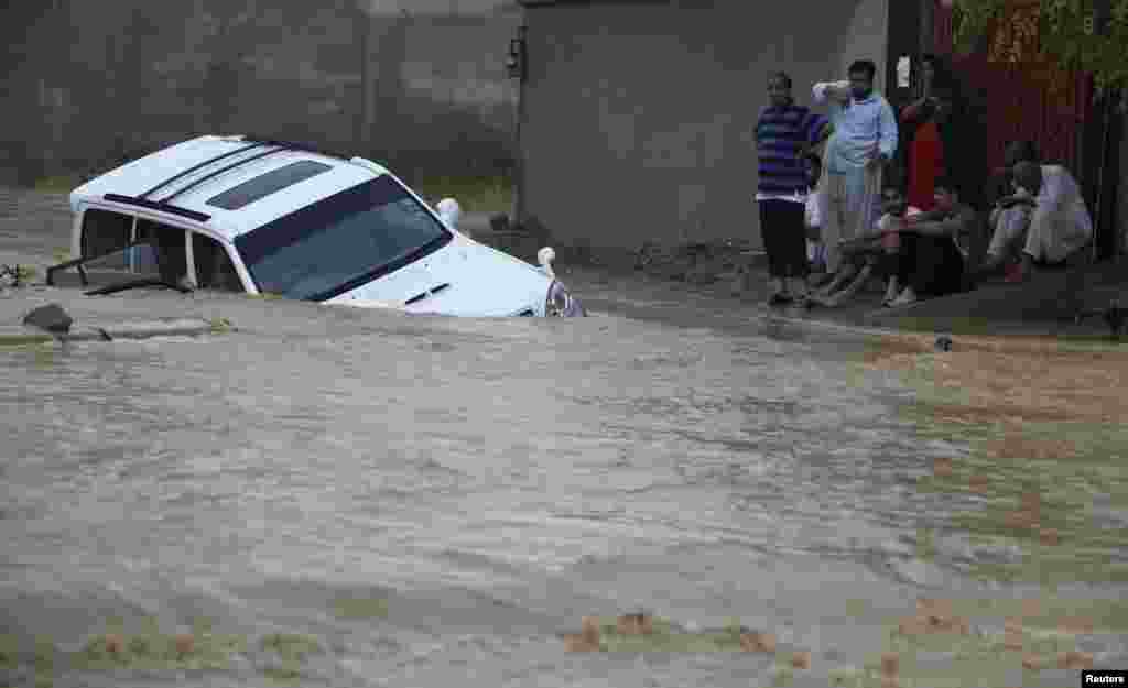 Family members wait for rescue workers after their vehicle was submerged in flood waters on the outskirts of Karachi, August 4, 2013.&nbsp;