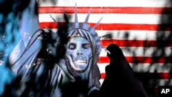 FILE - An Iranian woman walks past graffiti art characterizing the U.S. Statue of Liberty, painted on the wall of the former US embassy in Tehran, Iran, Sept. 25, 2007. 