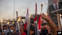 Anti-government protesters hold torches as they light a flame over a metal statue that reads in Arabic "October 17, Revolution," next to the site of the Aug. 4 blast in the seaport of Beirut that killed scores, in Beirut, Lebanon, Oct. 17, 2020.