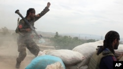 FILE - An Afghan National Army soldier, left, shouts at Taliban fighters after firing a rocket toward Taliban positions, on the outskirts of Kunduz, northern Afghanistan, April 16, 2016.