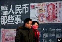 A couple walk past a display showing the security features of the new 100 Yuan note in Beijing, Jan. 11, 2016.