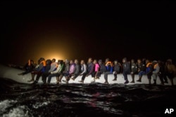 FILE - Refugees and migrants from many different African nationalities sit aboard an overcrowded rubber boat leaving Libyan territorial waters early March 5, 2017.