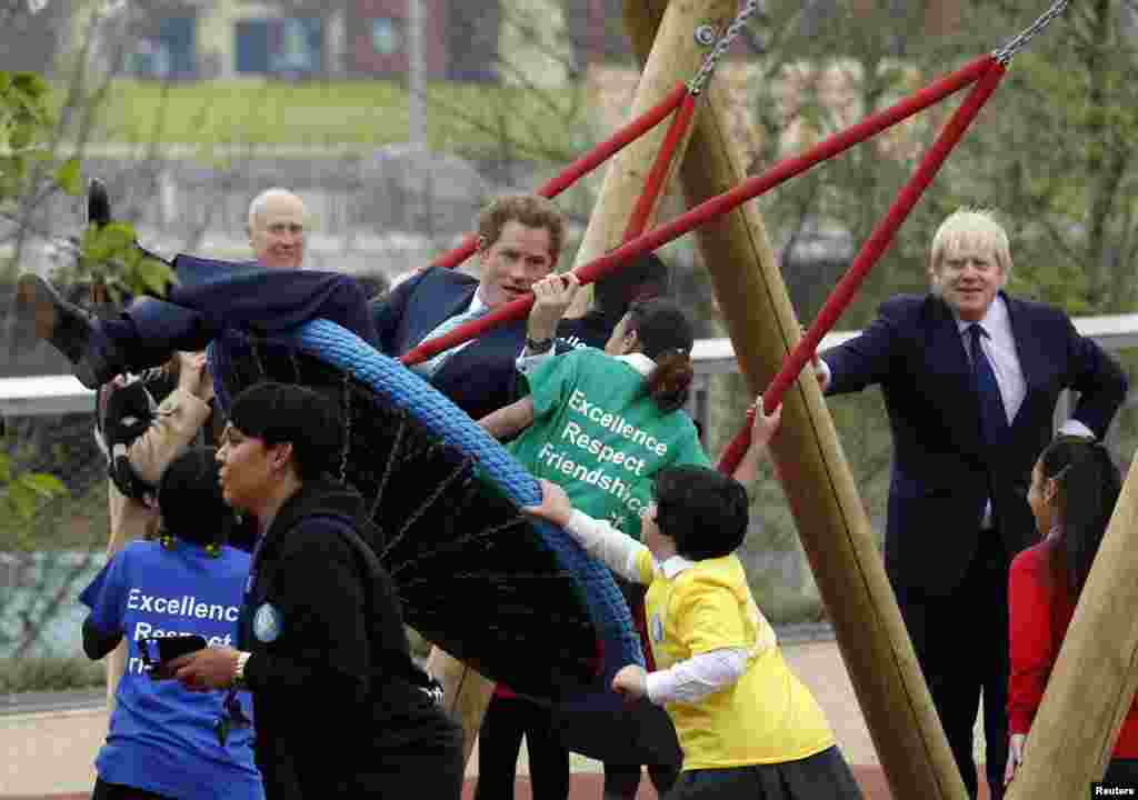 Pangeran Harry dari Inggris bermain ayunan dengan anak-anak sementara walikota London Boris Johnson (kanan) mengamati mereka, dalam sebuah acara kunjungan ke Taman Olimpik Ratu Elizabeth sebelum pembukaan taman itu pada tanggal 5 April 2014, di Stratford di London Timur. &nbsp;