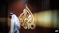 FILE - An employee of the Qatar-based Al-Jazeera network passes by an Al-Jazeera logo at the network's offices in Doha, Qatar.