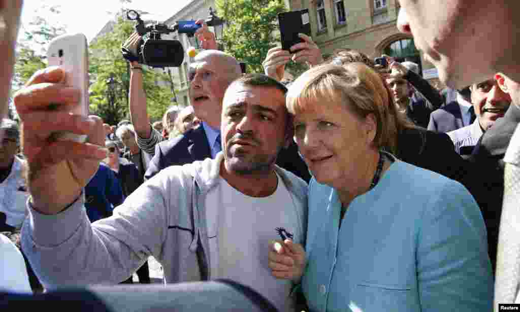 German Chancellor Angela Merkel visits a refugee camp near the Federal Office for Migration and Refugees at Berlin&#39;s Spandau district. A migrant takes a selfie with Merkel outside the refegee camp.