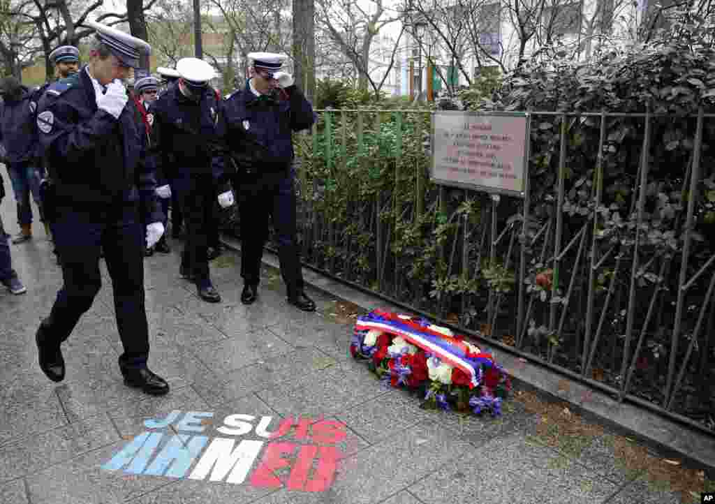 Policemen walk past spray paint on the sidewalk reading: &quot;Je suis Ahmed,&quot; or &quot;I am Ahmed,&quot; in the red, white and blue of the French flag near a plaque commemorating late police officer Ahmed Merabet in Paris, Tuesday Jan. 5, 2016.
