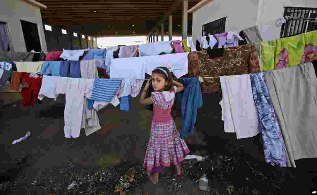 Seorang anak perempuan Suriah mengawasi pakaian-pakaian yang dijemur di kamp pengungsi di kota Azaz, Suriah (26/8).